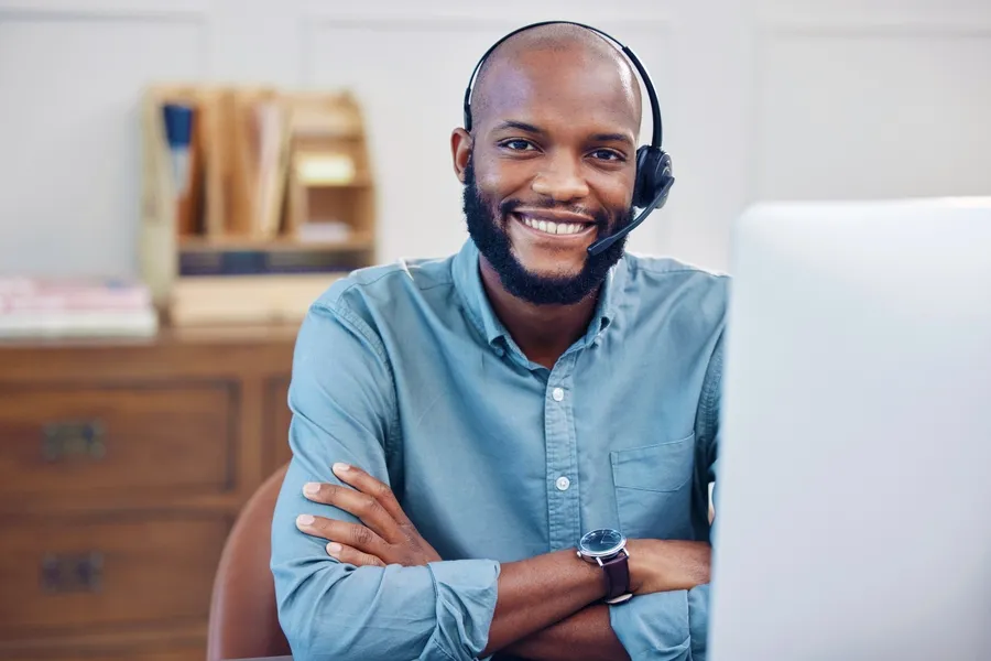 Remote Computer Repair Technician At His All In One Computer Smiling At The Camera Wearing A Headset